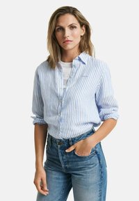 Camicia a righe blu e bianche, in tessuto leggero, con maniche arrotolate, abbinata a jeans blu a vita alta con taschino frontale.