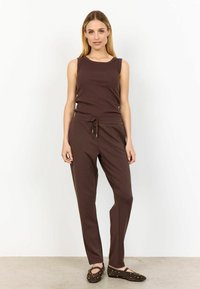Bruine tanktop en bijpassende joggers gemaakt van zachte stof, met een trekkoord in de taille en een gladde textuur. Ballerina's met studs maken de outfit compleet.