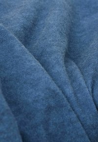 Weicher blauer Stoff mit einem feinen, strukturierten Strick. Das Material wirkt leicht und leicht samtig, mit sichtbaren, geschichteten Falten und Drapierungen.