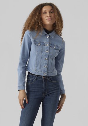 Chaqueta de mezclilla azul claro con cuello, cierre de botones al frente y dos bolsillos en el pecho. Presenta mangas largas y un corte cropped, combinada con jeans azul oscuro.