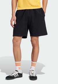 Black athletic shorts with elastic waistband, lightweight textured fabric, paired with white socks featuring orange stripes and black sneakers.