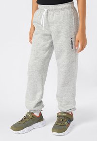 Grijze sweatpants met een elastische tailleband en trekkoord, met een zwart "Champion" logo. Gecombineerd met olijfgroene sneakers met witte zolen.