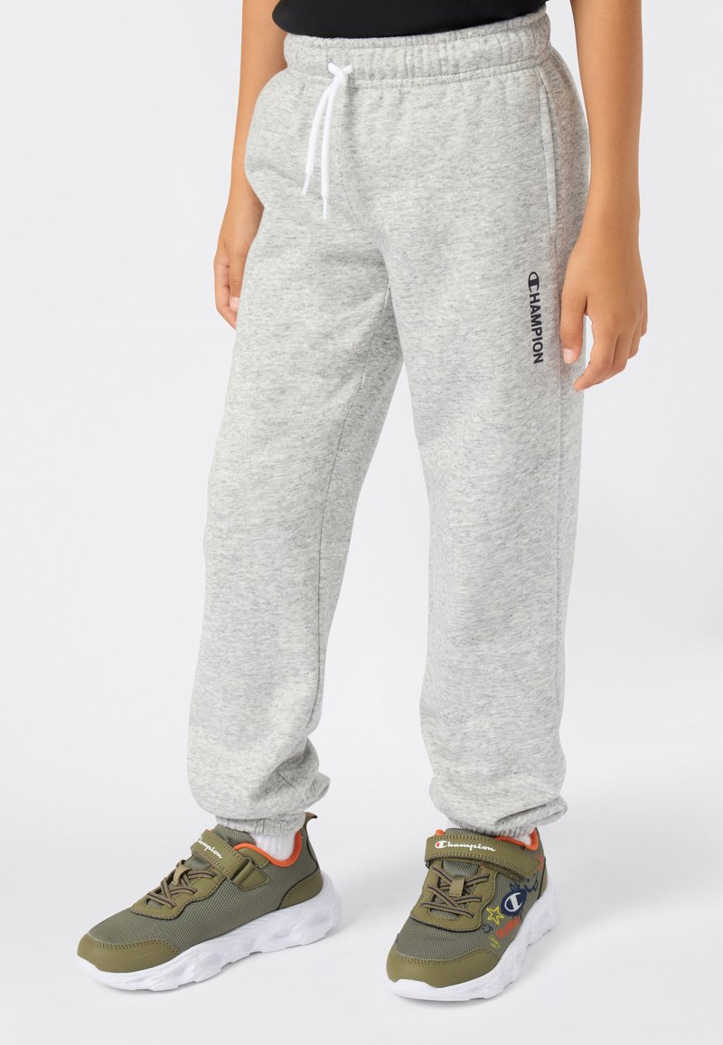 Grijze sweatpants met een elastische tailleband en trekkoord, met een zwart "Champion" logo. Gecombineerd met olijfgroene sneakers met witte zolen.