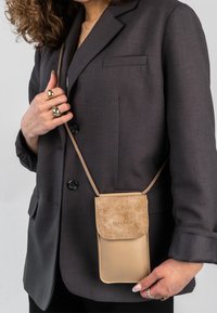 Pochette portatelefono a tracolla beige realizzata in materiali lisci e testurizzati, con patta pieghevole e tracolla a catena metallica.