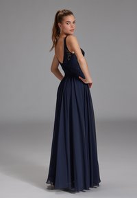 Abito lungo blu navy con un bustino in pizzo aderente, schiena scoperta e gonna fluente. Tessuto fluido, con delicati dettagli in pizzo sulla parte superiore.