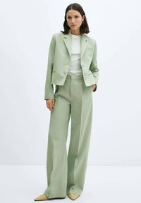 Light green tailored suit with a cropped blazer and wide-leg trousers, made of smooth fabric, paired with a white top and pointed beige shoes.