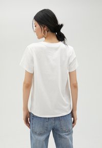 Camiseta de algodón blanca con mangas cortas, escote redondo y un corte relajado. Se lleva con unos vaqueros azules de cintura alta, mostrando una textura suave.