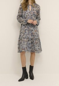 Kwiatowa sukienka w jasnoniebieskim materiale, z długimi rękawami, dekoltem w kształcie łezki i spódnicą z falbanami. Noszona z czarnymi botkami za kostkę.