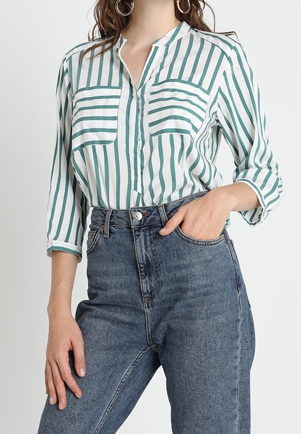 Blusa a righe verdi e bianche con maniche lunghe, due tasche sul petto e colletto, abbinata a jeans in denim blu a vita alta.