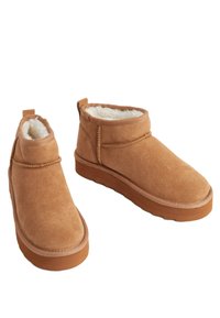 Bottines en daim beige avec une douce doublure en fourrure blanche, bout arrondi et semelle en caoutchouc brun. Design décontracté avec une forme simple.