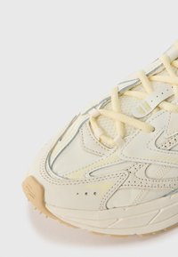 Lichtgekleurde sneaker met een gestructureerde bovenkant, meshpanelen en rubberen zool. Accenten met neutrale stiksels en veters.