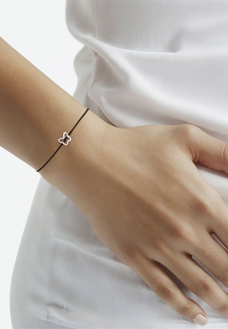 Melnas virvītes aproce ar sudraba tauriņa piekariņu. Piekariņš ir izrotāts ar pulētu apdari, ko papildina gluda ādas krāsa.