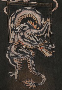 Tela vaquera negra con un gran dragón intrincadamente bordado en tonos de gris y naranja, con escamas detalladas y garras afiladas.