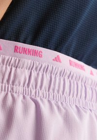 Lichtpaarse hardloopshorts hebben een gestructureerde tailleband met de tekst "RUNNING" in het roze. De stof is zacht met een geplooide elastische uitstraling.
