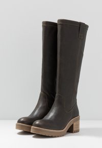 Hnědé kožené vysoké boty ke kolenům s texturovaným povrchem, zaoblenými špičkami a vrstvenými dřevěnými podpatky. Vyznačují se jemným prošíváním a ozdobou u kotníku.