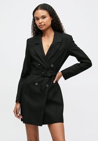 Czarna sukienka-blazer w paski z głębokim dekoltem w kształcie V, podwójnymi guzikami i paskiem w talii. Długie rękawy i dopasowany krój.