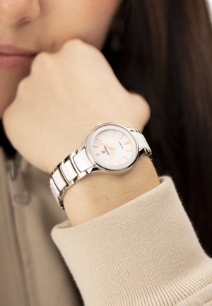 Person resting chin on fist, wearing a stainless steel wristwatch with a white dial and minimalist design.