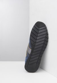 Scarpa blu e grigia con suola in gomma testurizzata, dettagli gialli e un motivo a zigzag per migliorare la presa. Il design è snello e moderno.