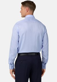 Svetlo modrá károvaná košeľa s dlhými rukávmi, so zapínaním na gombíky, kontrastnými manžetami, nosená s tmavými nohavicami a čiernym opaskom.