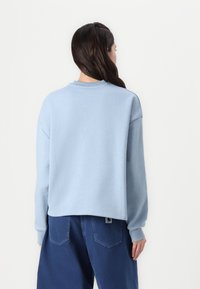 Helles blauer Sweatshirt mit Rundhalsausschnitt und überschnittenen Schultern, aus weichem Material gefertigt. Dazu passen dunkelblaue weit geschnittene Hosen mit einem Logopatch.