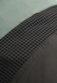 Gros plan sur des sections de tissu présentant un tricot vert lisse, un tricot gaufré noir texturé et des matériaux gris foncé lisses cousus ensemble avec des coutures visibles.
