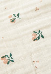 Tissu en coton de couleur crème avec un motif de grille texturé. Présente des broderies florales dans des tons pêche et vert.