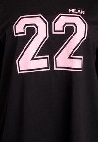 Black T-shirt featuring large pink numbers "22" and the word "MILAN" above, with a simple, clean design and contrasting colors.