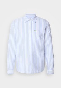 Chemise à manches longues boutonnée avec des rayures verticales bleu clair et blanc et un petit logo crocodile vert sur la poche poitrine gauche.