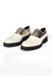 Chaussures en cuir blanc avec une partie supérieure texturée en or, semelles en caoutchouc noir et lacets noirs. Bout arrondi avec une finition lisse.