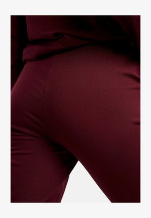 Leggings bordeaux en tissu extensible, dotés d'une texture lisse et d'une coupe ajustée qui épouse la forme du corps.