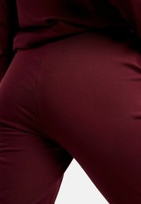 Legíny bordovej farby z pružnej látky, s hladkým povrchom a priliehavým strihom, ktorý kopíruje tvar tela.