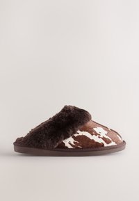 Kapcie o brązowo-białym wzorze w kształcie cętek, z puszystą ciemnobrązową opaską, zaokrąglonym kształtem i płaską podeszwą. Miękka futrzana tekstura kontrastuje z gładką powierzchnią.