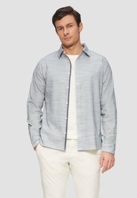 Lichtblauw gestippeld overhemd met lange mouwen, voorzien van een witte onderhemd en beige broek. Eenvoudige kraag en subtiele textuur.