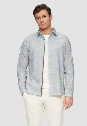 Lichtblauw gestippeld overhemd met lange mouwen, voorzien van een witte onderhemd en beige broek. Eenvoudige kraag en subtiele textuur.