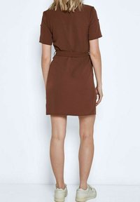 Hnědress krátké rukávy s páskem v pase, hladká textura a délka ke kolenům, v kombinaci se světle zbarvenou obuví.