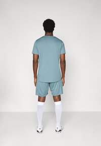 Teal athletic shirt and shorts with a loose fit, paired with white knee-high socks and black-and-white cleats. Simple design with no patterns.