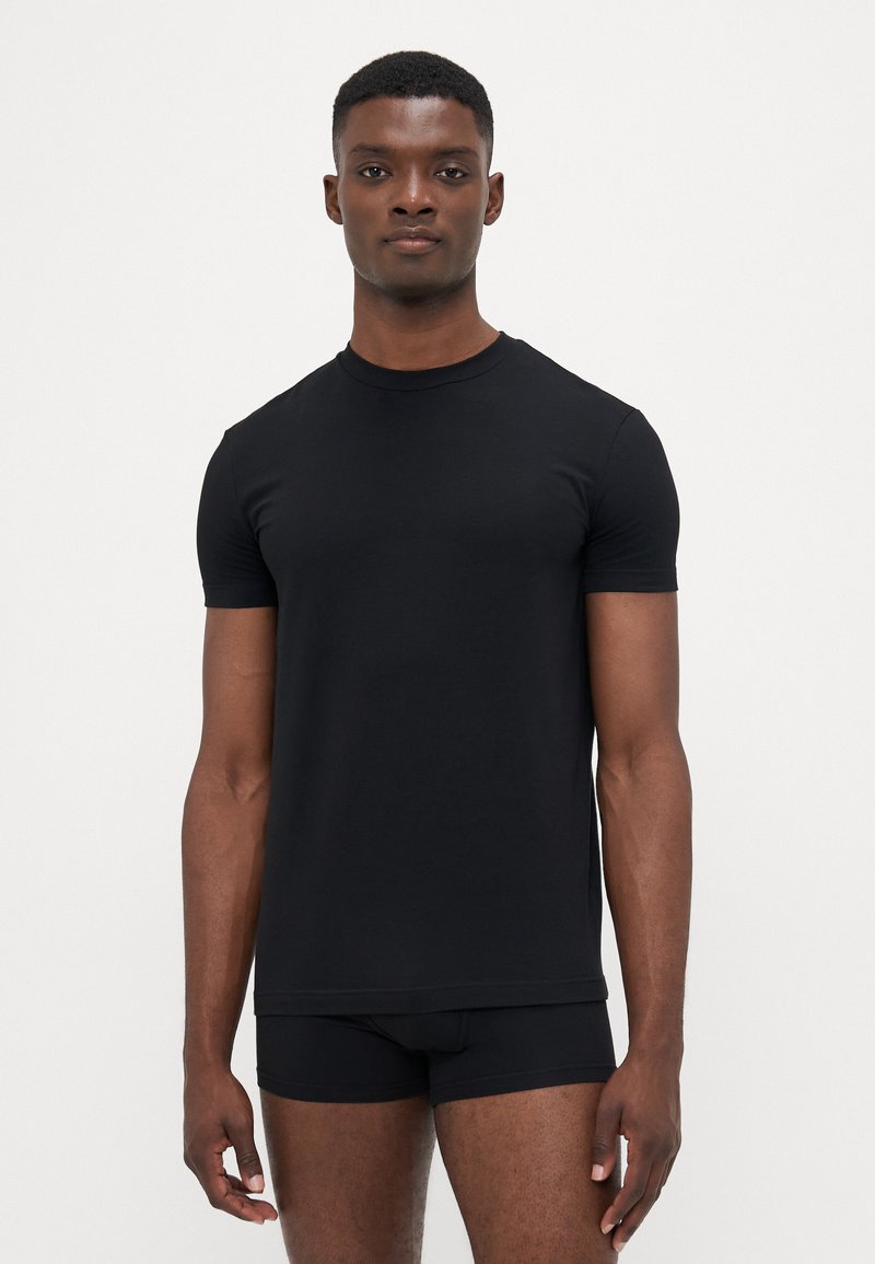 Schwarzes Kurzarm-T-Shirt aus glattem Baumwolljersey, mit Rundhalsausschnitt und taillierter Passform. Das Modell steht frontal mit schwarzen Boxershorts.