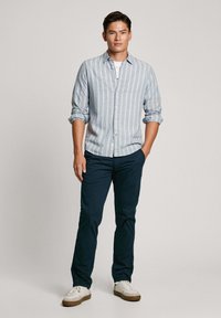 Svetlo modra črtasta srajca na gumb, mornarsko modri hlače in bele superge. Srajca ima zavihane rokave in sproščen kroj.