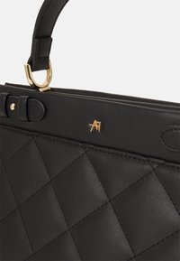 Musta tikattu nahkakäsilaukku, jossa on rakenteellinen muotoilu, kultaiset metalliosat ja yläkädensija, jossa on soljella varustettu sulkemismekanismi.