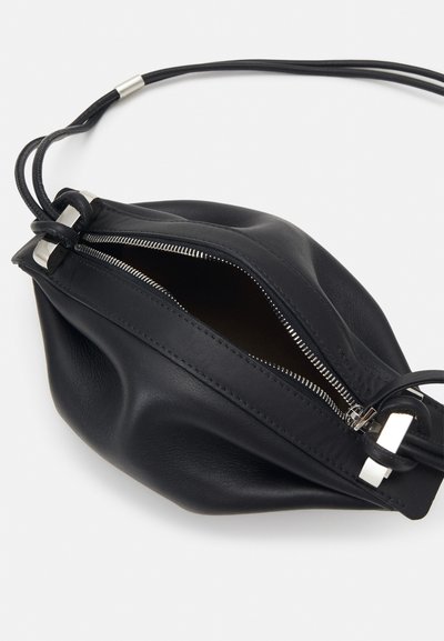 Pochette en cuir noir avec fermeture éclair argentée partiellement ouverte et cordons noirs sur fond blanc.