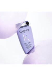 Lavendel Kérastase Blond Absolu Shampoo-Flasche, die zwischen zwei hellvioletten Luftballons auf weißem Hintergrund lehnt.