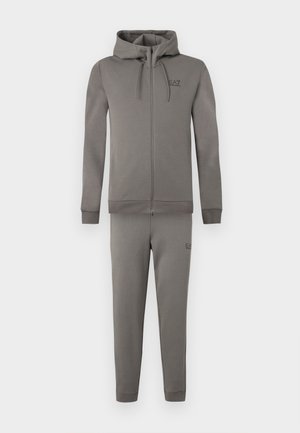 Sudadera con capucha gris con cremallera y pantalones deportivos a juego en tela suave. Cuenta con capucha, detalle de logo y puños acanalados. Diseño simple y estilizado.