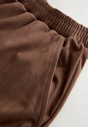 Braune Jogginghosen aus weichem Stoff mit elastischem Bund und unauffälliger Seitentasche, teilweise zu sehen.