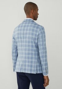 Jasnoniebieska marynarka w kratę z wyłogami, pojedynczym rozcięciem i guzikami na mankietach, wykonana z teksturowanej tkaniny.