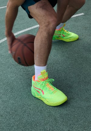 Le scarpe da basket alta in verde neon presentano un motivo testurizzato, accenti rosa, lacci brillanti e una suola flessibile. Un pallone da basket è in gioco.
