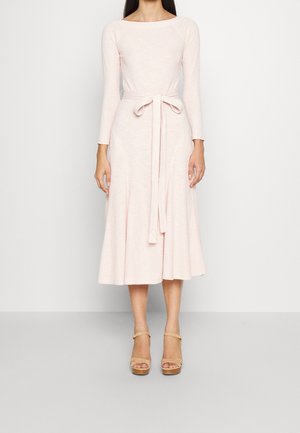 Jasnoróżowa midi sukienka z długimi rękawami, dopasowanym gorsetem i wiązanym w pasie. Gładka tekstura i rozkloszowany krój spódnicy. W połączeniu z beżowymi sandałami na obcasie.