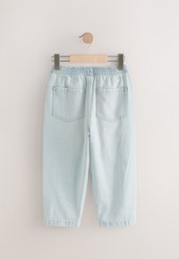 Hellblaue Jeanshose mit elastischem Bund, schmal zulaufendem Schnitt, zwei Gesäßtaschen und ausgefransten Saumdetails. Hängt an einer Holzklammer.