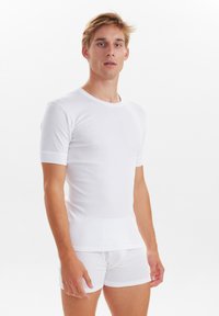 Hvid kortærmet t-shirt lavet af glat stof, parret med hvide boxershorts. Begge har en tætsiddende design og kontrasterende teksturerede kanter.