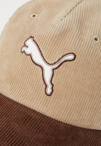 Corduroy cap featuring a beige upper and dark brown visor, with a white embroidered Puma logo prominently displayed.