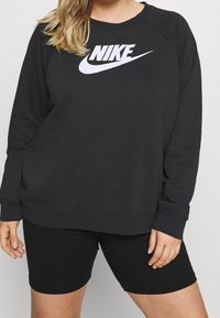 Svart sweatshirt i mjukt tyg med en vit Nike-logotyp, med rund halsringning och långa raglanärmar, kombinerad med svarta shorts.